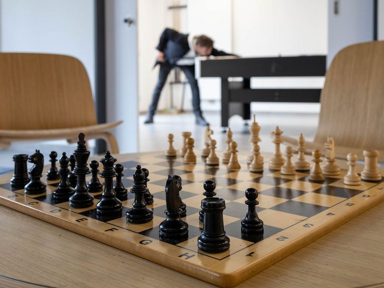 Ein Schachspiel im Vordergrund - im Hintergrund spielt ein Mann Billiard