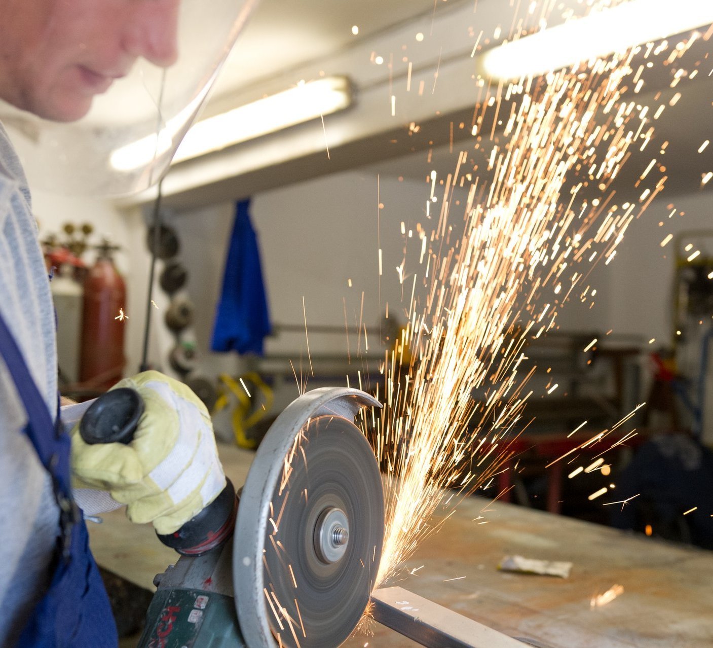 Metallwerkstatt: ein Mann in Schutzkleidung lässt mit der Flex die Funken sprühen