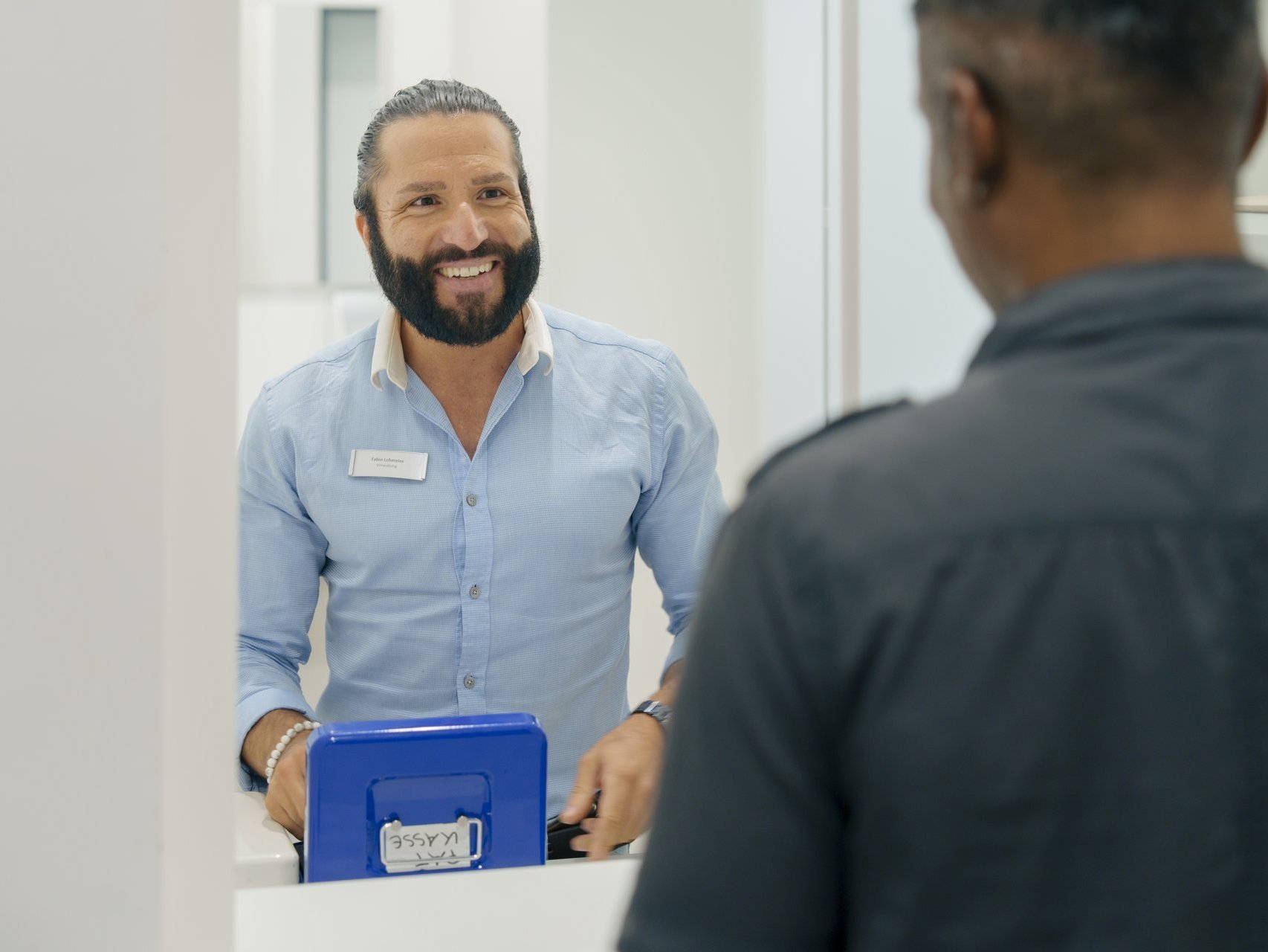 Ein Mann arbeitet an der Kasse und laechelt seinen Kunden an