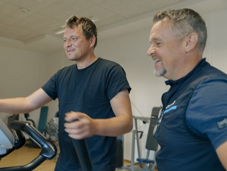 Ein Mann trainiert mit einem Geraet im Fitnessstudio und laesst sich beraten 1