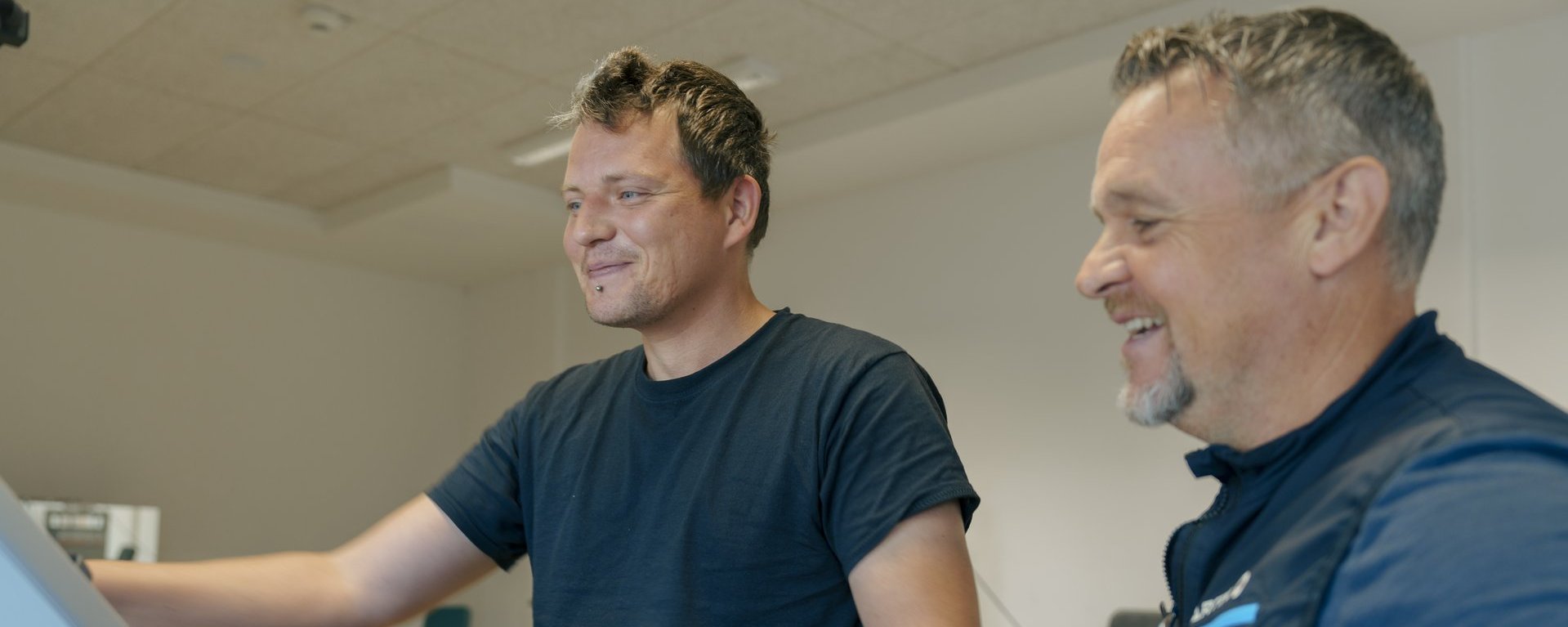 Ein Mann trainiert mit einem Geraet im Fitnessstudio und laesst sich beraten 1