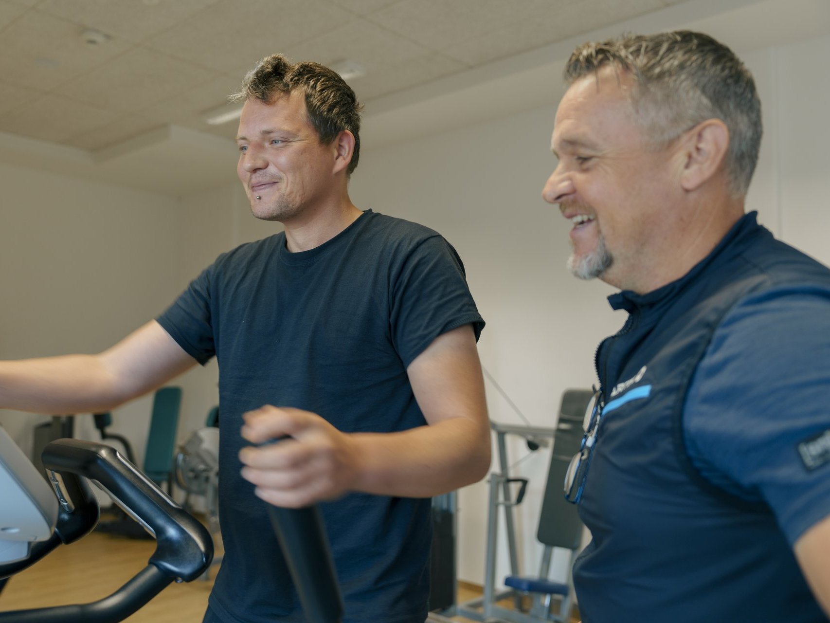 Ein Mann trainiert mit einem Geraet im Fitnessstudio und laesst sich beraten 1