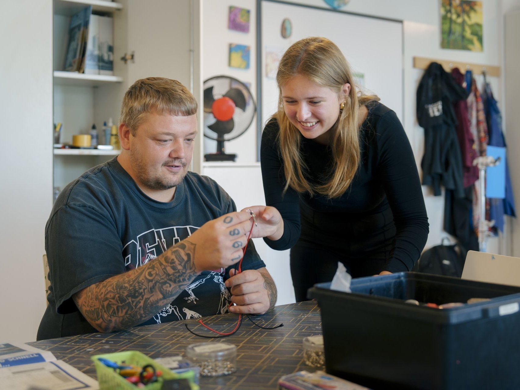 Eine Frau zeigt einem Mann wie man ein Armband knüpft