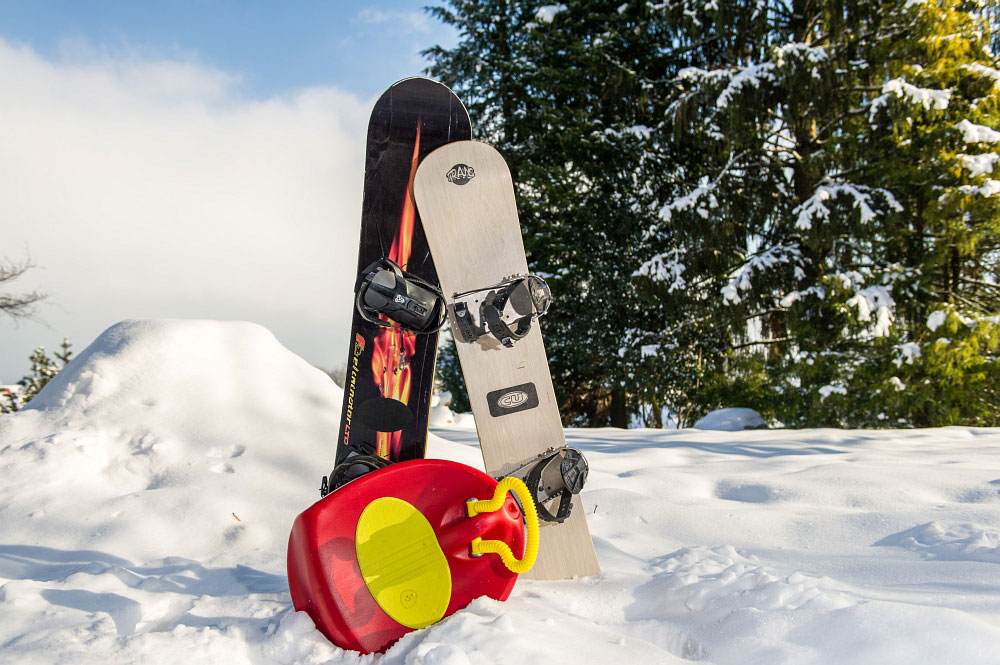 zwei Snowboards und ein Kinder-Rodel aus Plastik im Schnee